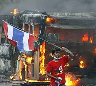 A supporter of former Thai Prime Minister Thaksin Shinawatra waves a national flag in front of a torched bus during a protest in Bangkok