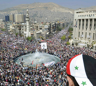 Youth with Syrian flag on hat watches crowd