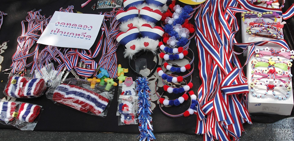                 cc Timo Kozlowski, modified, Fashion accessories in the colours of the Thai flag are signature of anti-government protesters during Bangkok Shotdown in January 2014. / https://commons.wikimedia.org/wiki/File:Bangkok_Shutdown_-_Protest_Memorabilia_02.JPG
              