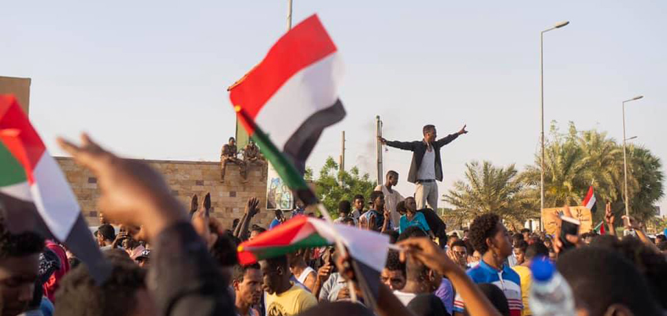 Sudan protests 2019, CC M. Saleh, modified, Wikicommons, https://commons.wikimedia.org/w/index.php?title=Special:Search&title=Special:Search&redirs=0&search=khartoum+protests&fulltext=Search&fulltext=Advanced+search&ns0=1&ns6=1&ns14=1&advanced=1&searchToken=1a26j4o5p9lklfiy2kh8biz98#%2Fmedia%2FFile%3ASudanese_protestors_chanting.jpg