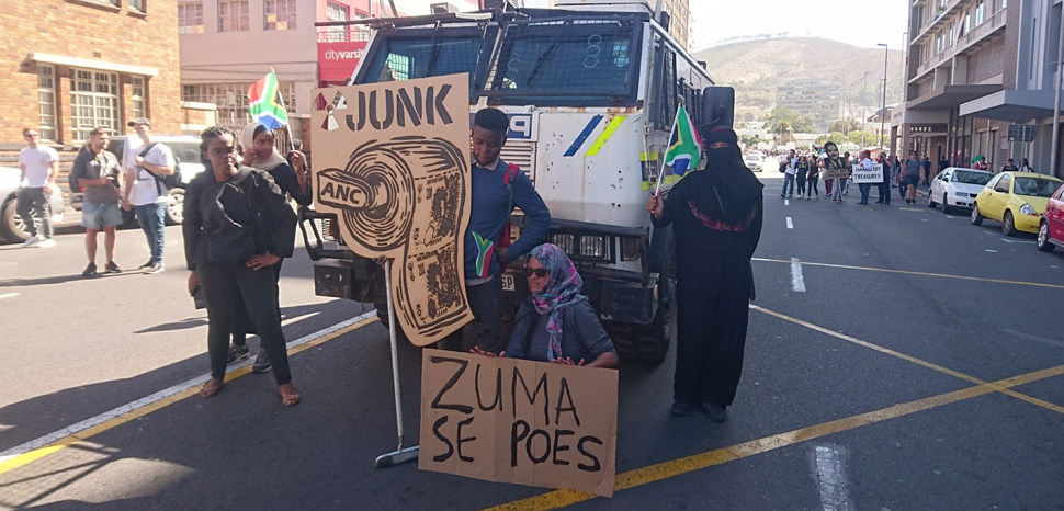 an anti-Zuma protest from 2017, cc Discott, modified, https://commons.wikimedia.org/w/index.php?title=Special:Search&title=Special:Search&redirs=0&search=president+zuma&fulltext=Search&fulltext=Advanced+search&ns0=1&ns6=1&ns14=1&advanced=1#/media/File:Anti-Zuma_protest_Cape_Town.jpg