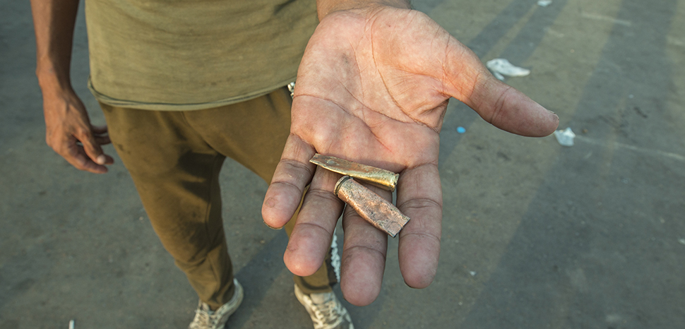 A man holds shells out as evidence of security forces using live ammunition against protesters in 2019; cc Mondalawy, modified, https://commons.wikimedia.org/wiki/File:%D8%A7%D8%AF%D9%84%D8%A9_%D8%B9%D9%84%D9%89_%D8%A7%D9%84%D8%B0%D8%AE%D9%8A%D8%B1%D8%A9_%D8%A7%D9%84%D8%AD%D9%8A%D8%A9_%D8%A7%D9%84%D9%85%D8%B3%D8%AA%D9%85%D8%AE%D8%AF%D9%85%D8%A9_%D8%B6%D8%AF_%D8%A7%D9%84%D9%85%D8%AA%D8%B8%D8%A7%D9%87%D8%B1%D9%8A%D9%86.jpg