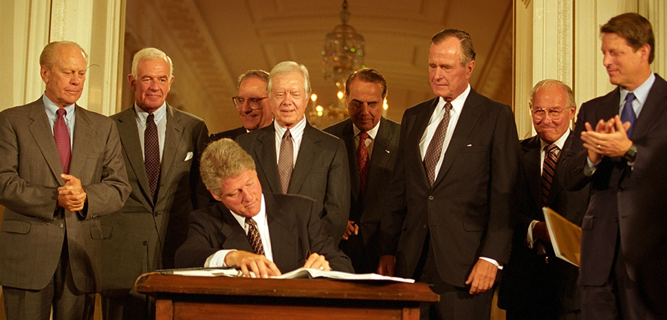 President Bill Clinton signs supplemental agreements to the North American Free Trade Agreement (NAFTA) ceremony in the East Room of the White House on September 14, 1993. He is joined by former President Gerald R. Ford, Representative Tom Foley, Senator George Mitchell, former President Jimmy Carter, Senator Bob Dole, former President George H.W. Bush, Representative William Ford and Vice President Albert Gore. cc Ralph Alswang, modified, https://commons.wikimedia.org/wiki/File:President_Bill_Clinton_signs_NAFTA.jpg